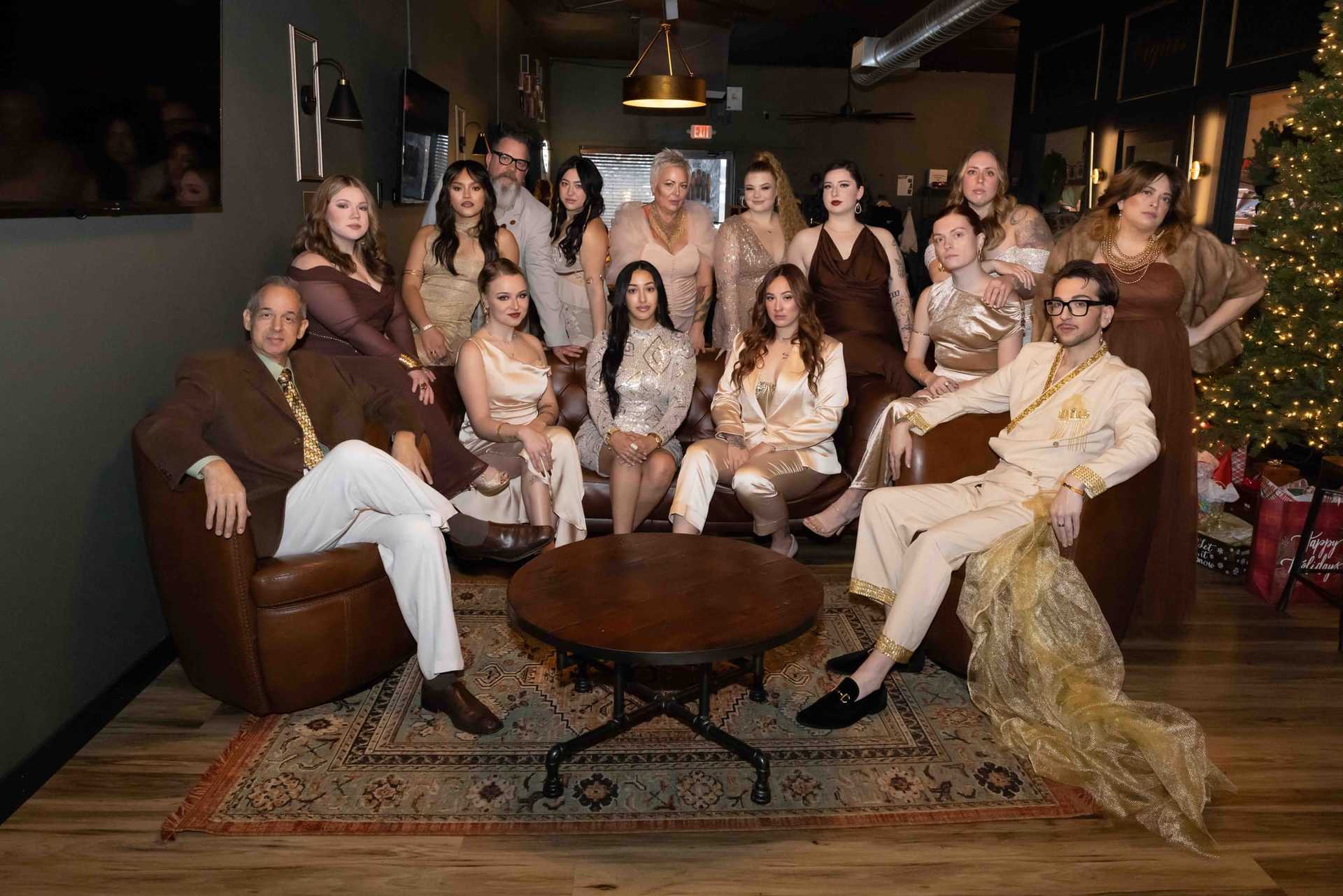 Group in elegant attire posing in a stylish room with soft lighting and a decorated Christmas tree.