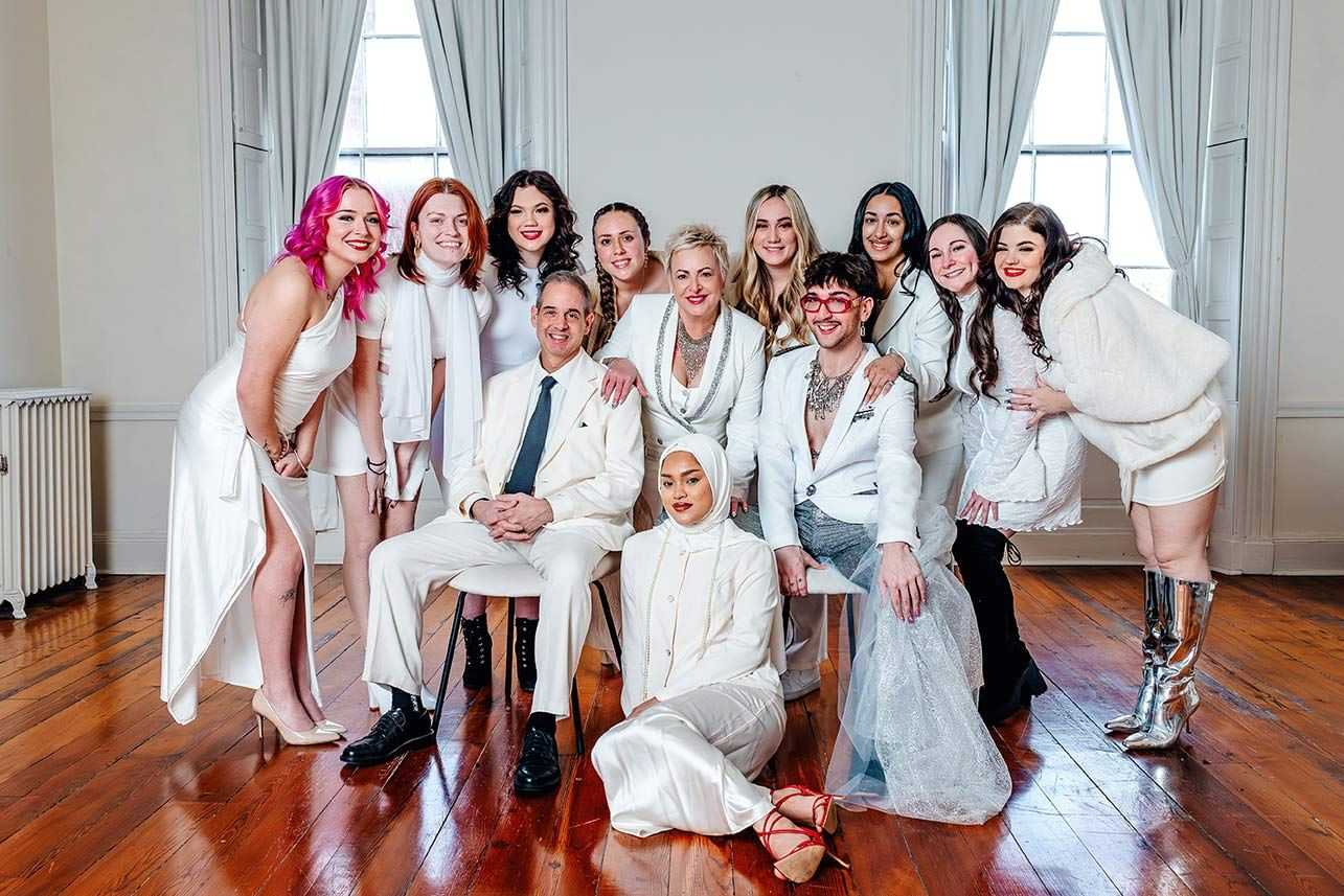 Group photo of people in white outfits, smiling in a bright room with wooden floors.